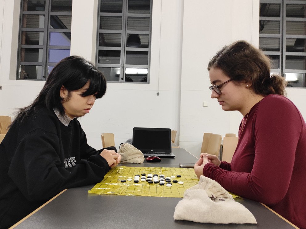 Zwei Personen sitzen sich gegenüber und Spelen das Go Spiel.