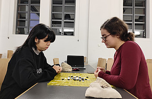 Zwei Personen sitzen sich gegenüber und Spelen das Go Spiel.